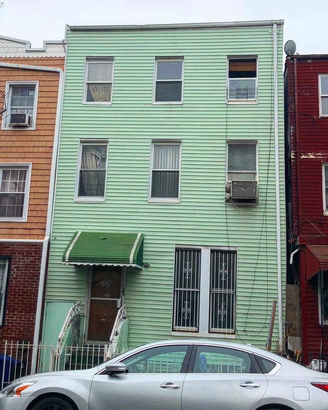 A Bed-Stuy rowhouse before purchase: mint green vinyl siding, a canvas awning and a window air conditioner